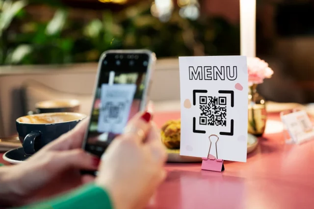 une femme scanne le qr code d'un menu dans un restaurant par le caméra d'un smartphone